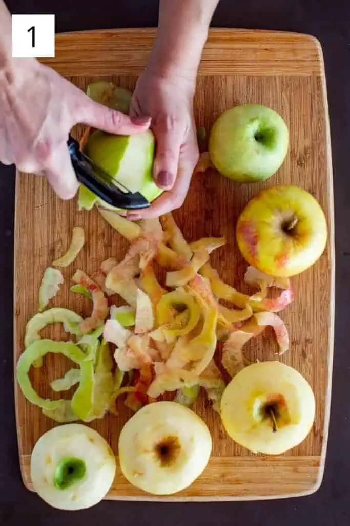 over head shot of hand peeling apples on wooden cutting board 