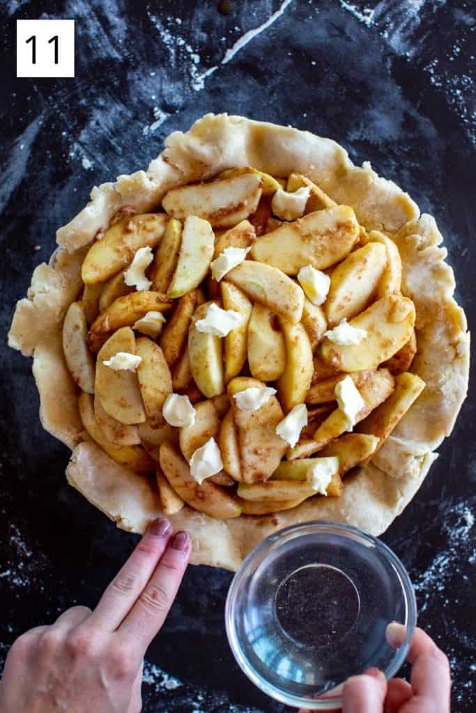 hands moistening the edges of the pie crust with water