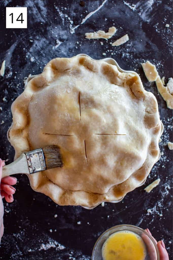 hand brushing the top of apple pie with egg wash