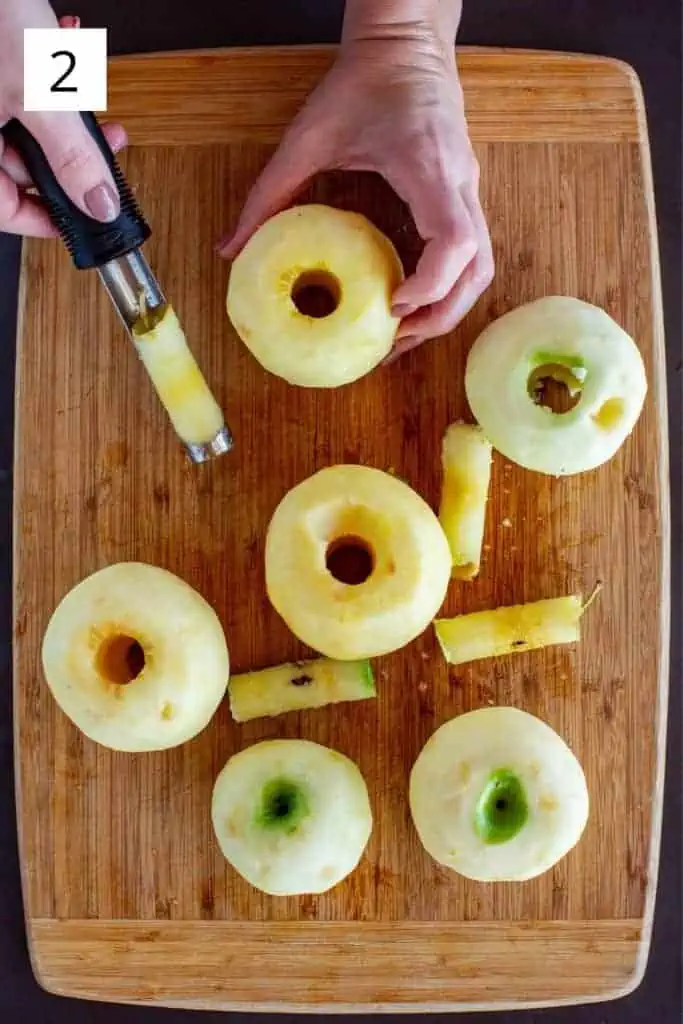 overhead shot of hand holding cored apple with apple corer on wood cutting board
