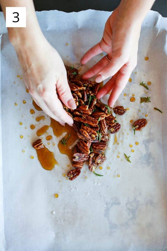 hands mixing pecans, maple syrup, rosemary and sea salt on a sheet pan