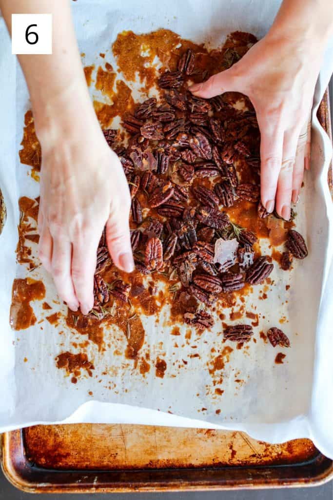 hands breaking up roasted pecans on a sheet pan