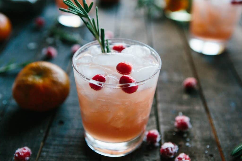 close up of Cranberry, Clementine + Rosemary cocktail with rosemary sprig sticking out and sugared cranberries in the foreground
