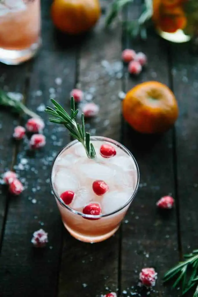 overhead shot of cocktail with sugared cranberries and a clementine on dark wooden background