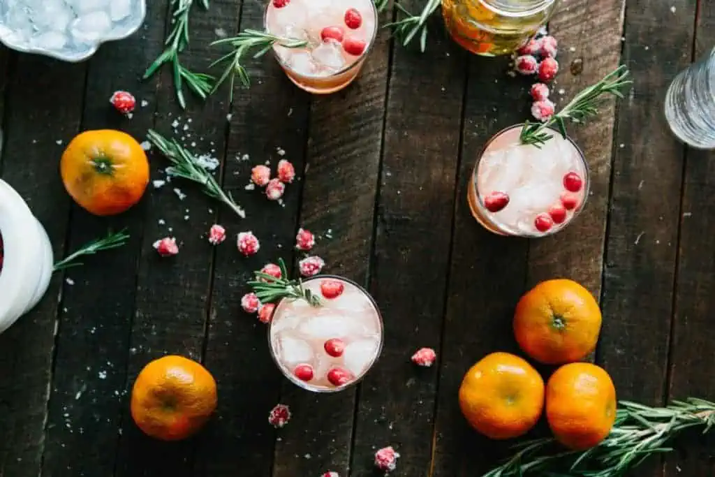 cocktails, clementines, sugared cranberries and rosemary sprigs on a dark wooden background