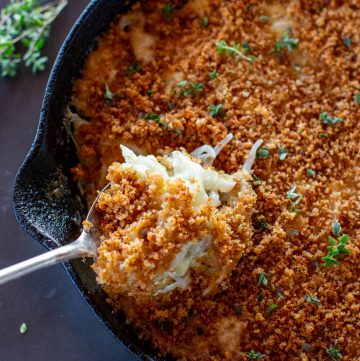 spoon full of fennel onion gratin in a cast iron skillet with fresh thyme