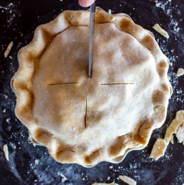 overhead shot of a hand cutting vents in an unbaked pie