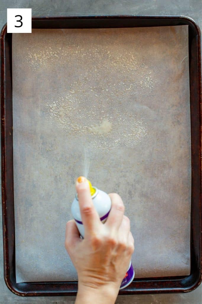 hand spraying a baking sheet with cooking spray