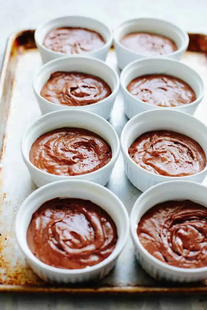 Six ramekins of unbaked flourless chocolate souffle on a baking sheet.