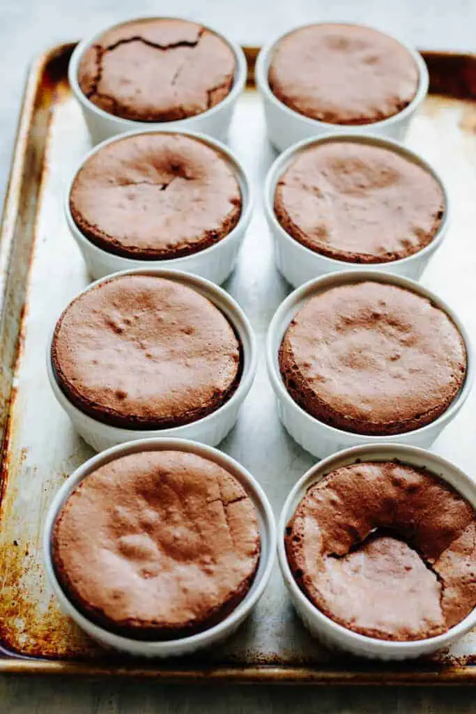 Six ramekins of baked flourless chocolate souffle on a baking sheet.