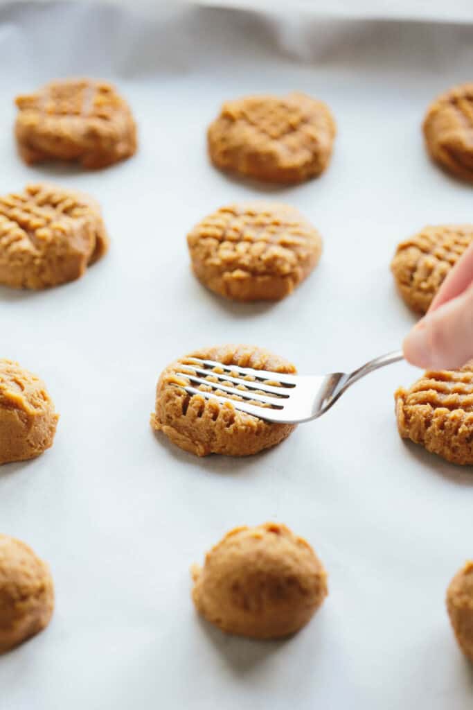 Pressing the tines of a fork into the classic crosshatch pattern on peanut butter cookie dough balls.