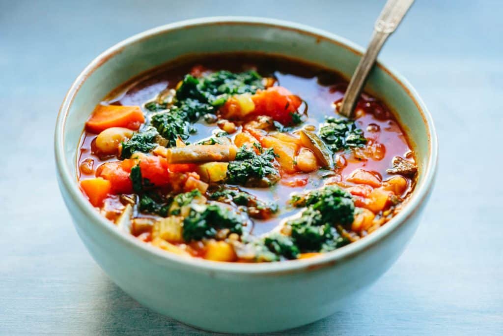 a bowl of vegetable minestrone soup with parsley pistou herb drizzle