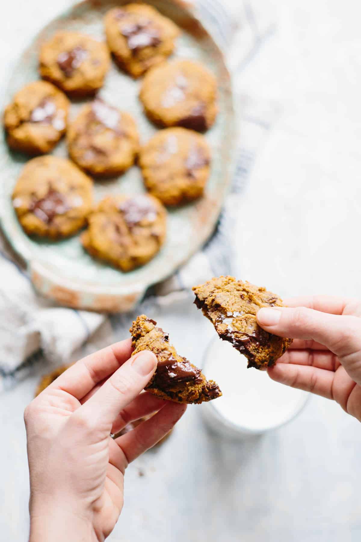 Close up of two hands holding two halves of a Paleo chocolate chip cookie.