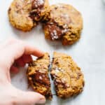 A hand breaking a Paleo chocolate chip cookie in half.