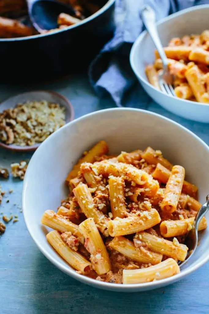 a bowl of rigatoni pasta with other bowls and plates in the background