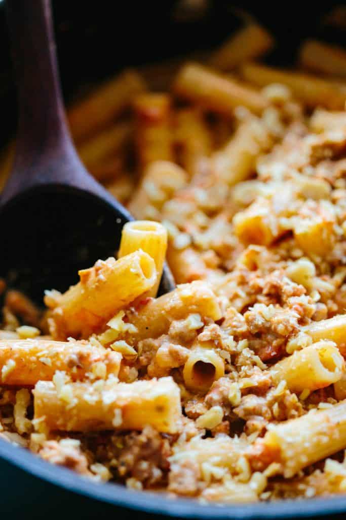 a close up of a wooden spoon mixing rigatoni with Italian sausage, mascarpone and walnuts