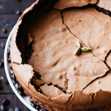 Top view of a flourless chocolate cake with a cracked top and cardamom pods