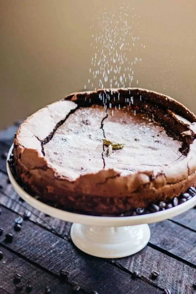 Powdered sugar falling on top of a chocolate cake on a cake stand.
