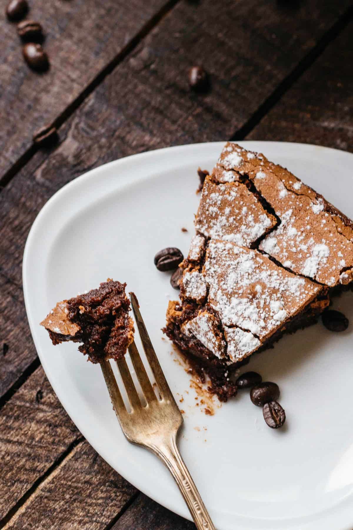 Top view of a slice of flourless chocolate cake on a white dessert plate with a fork holding a single bite.