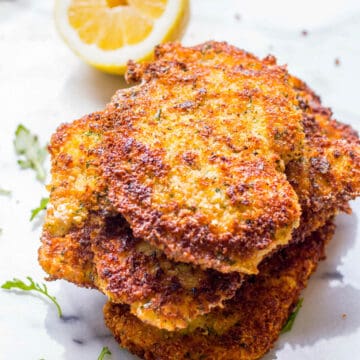 side view of a stack of thin breaded chicken breasts with a lemon