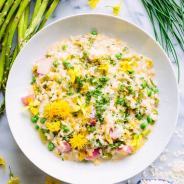 overhead shot of vegetable risotto with asparagus, chives, and rice scattered in the background