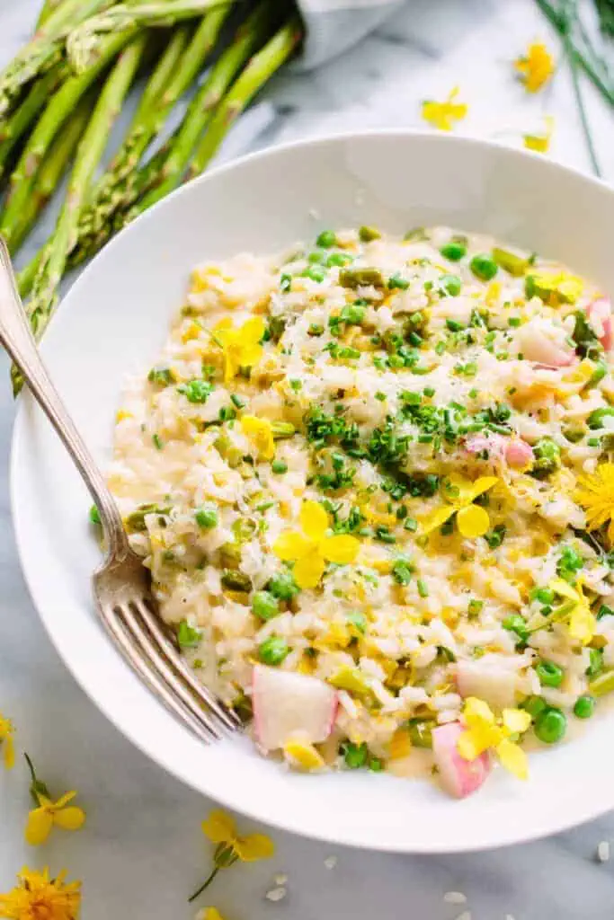 close up of spring risotto in a white bowl with a fork