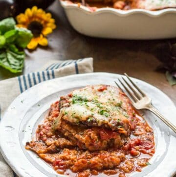 Side view of a plate of a serving eggplant parmesan with a fork.