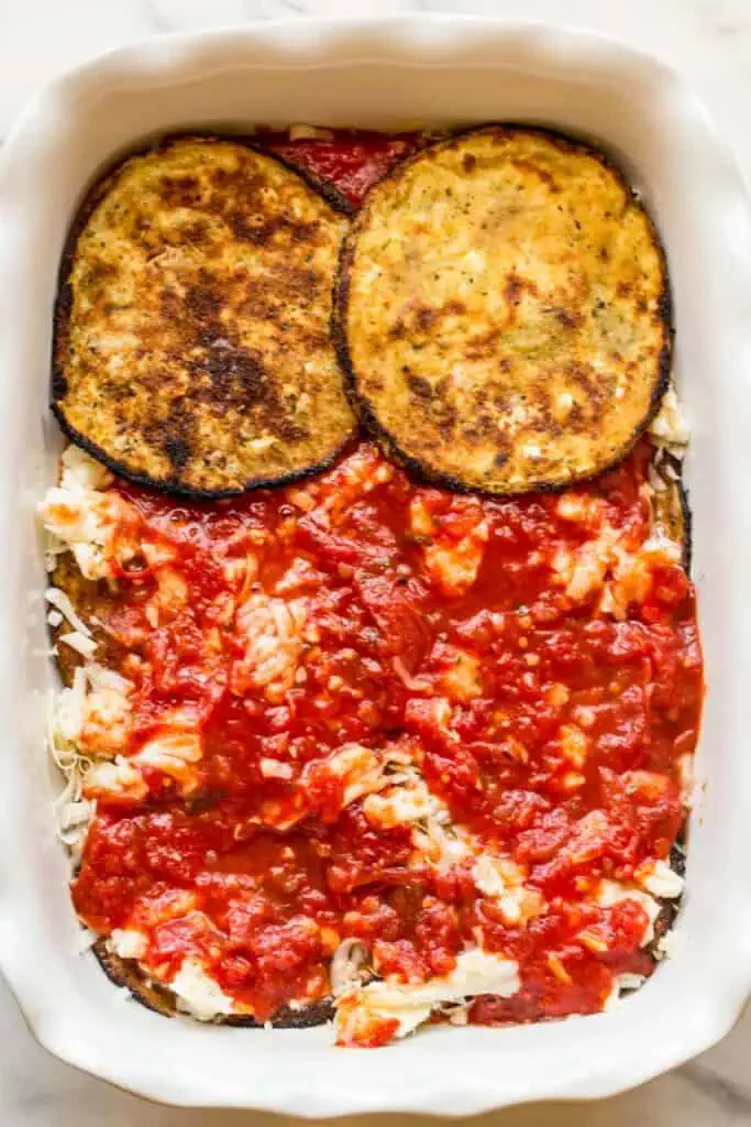 Sliced eggplant layered with cheese and pasta sauce in a white baking dish.