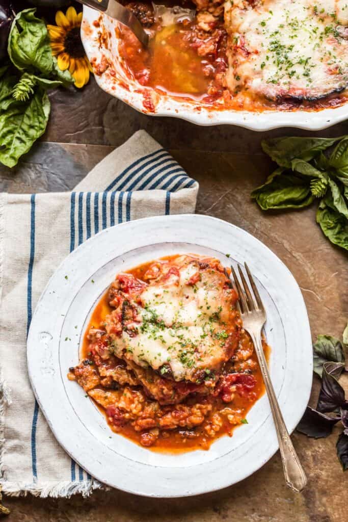 Top view of eggplant Parmesan in red sauce on a white dinner plate with a fork.