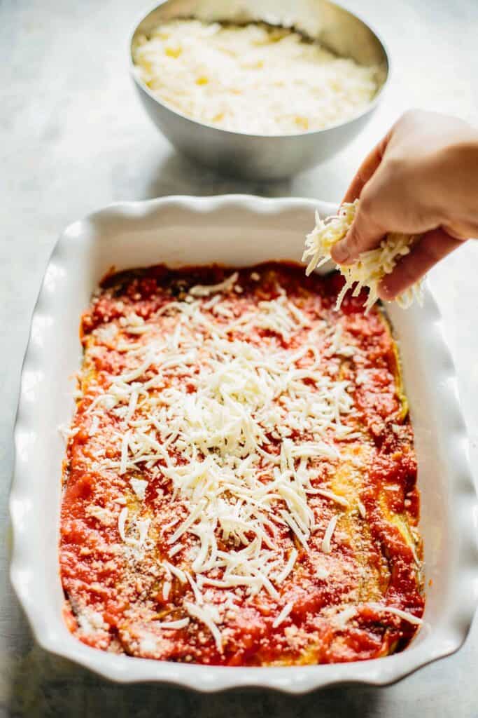 hand sprinkling cheese on an unbaked eggplant parmesan casserole