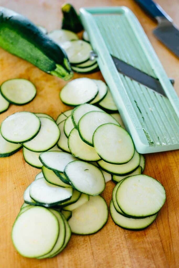 A mandolin next to a pile of thinly sliced zucchini rounds.