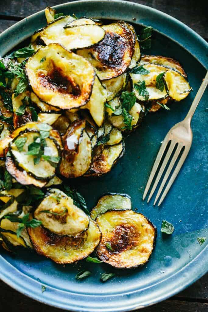 Close up of a serving dish full of thinly sliced and roasted zucchini.