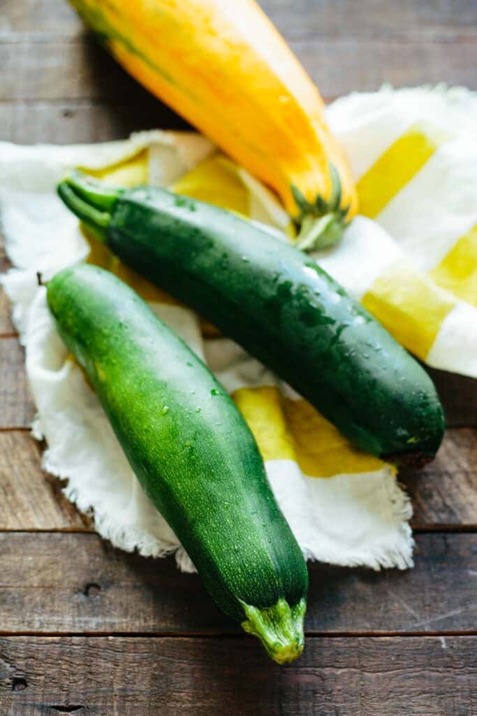 Three zucchini resting on a dishtowel on a wooden table.