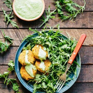 Plate loaded with salad greens and quinoa falafel drizzled with green tahini.