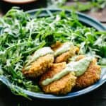 Plate filled with salad greens next to quinoa falafel drizzled with green tahini.