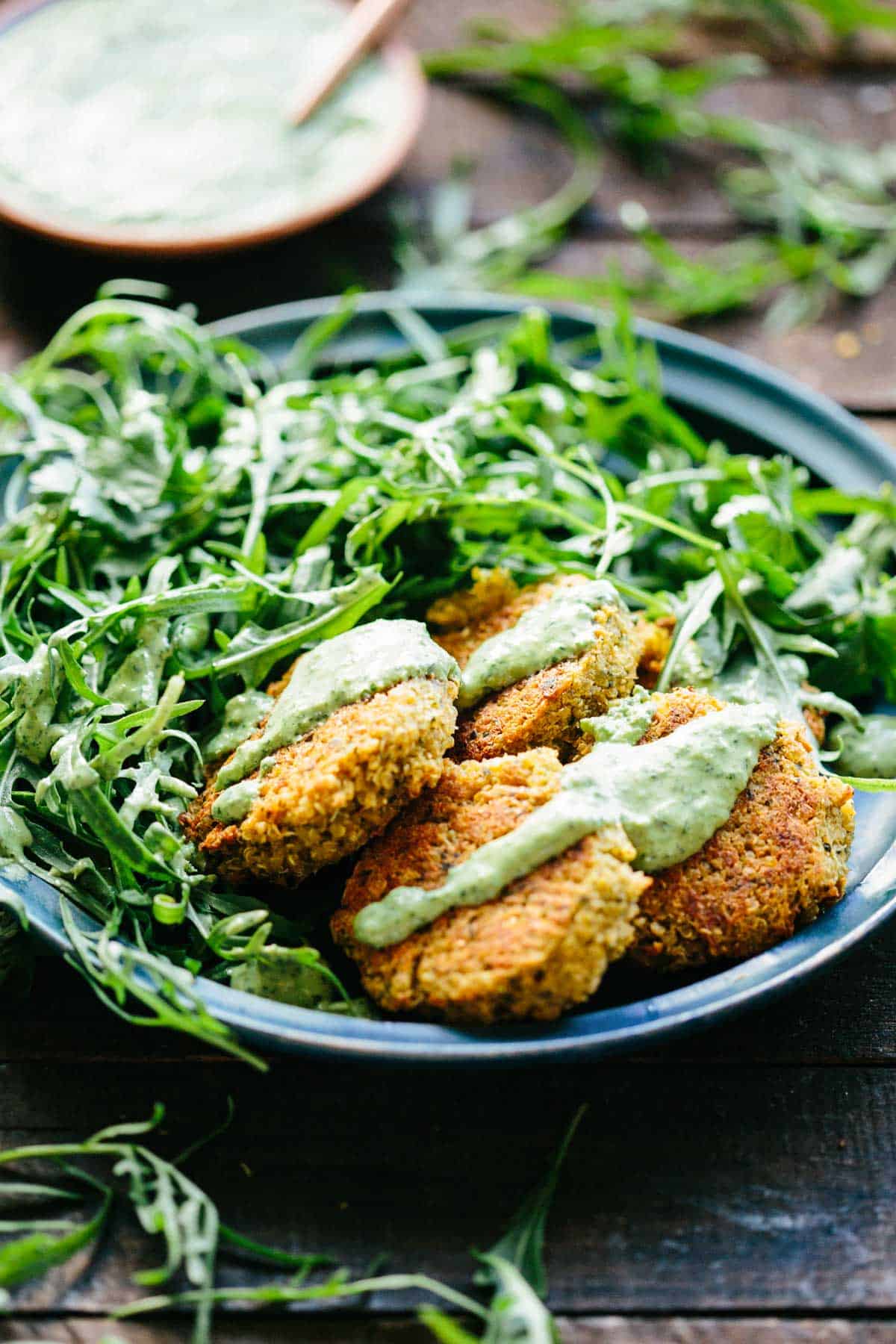 Plate filled with salad greens next to quinoa falafel drizzled with green tahini.