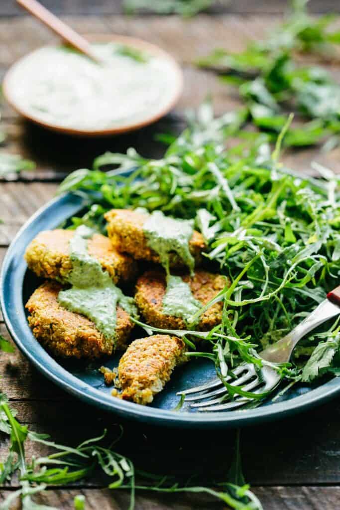 Plate of falafel patties dolloped with green tahini, next to salad greens and a fork.