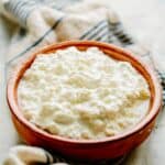 A red stoneware bowl filled with homemade ricotta cheese.