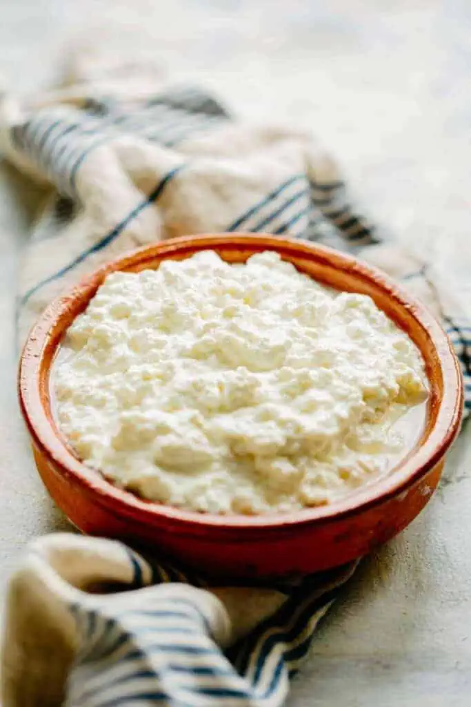 A red stoneware bowl filled with homemade ricotta cheese.