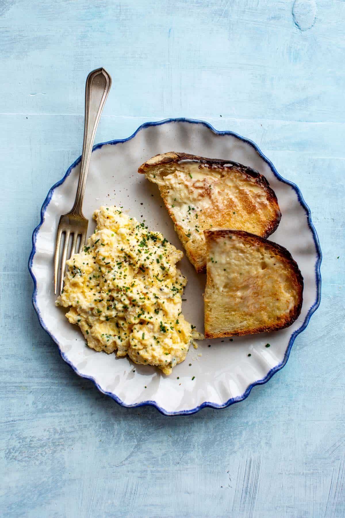 overhead shot of a plate with soft scrambled eggs and toast with a fork