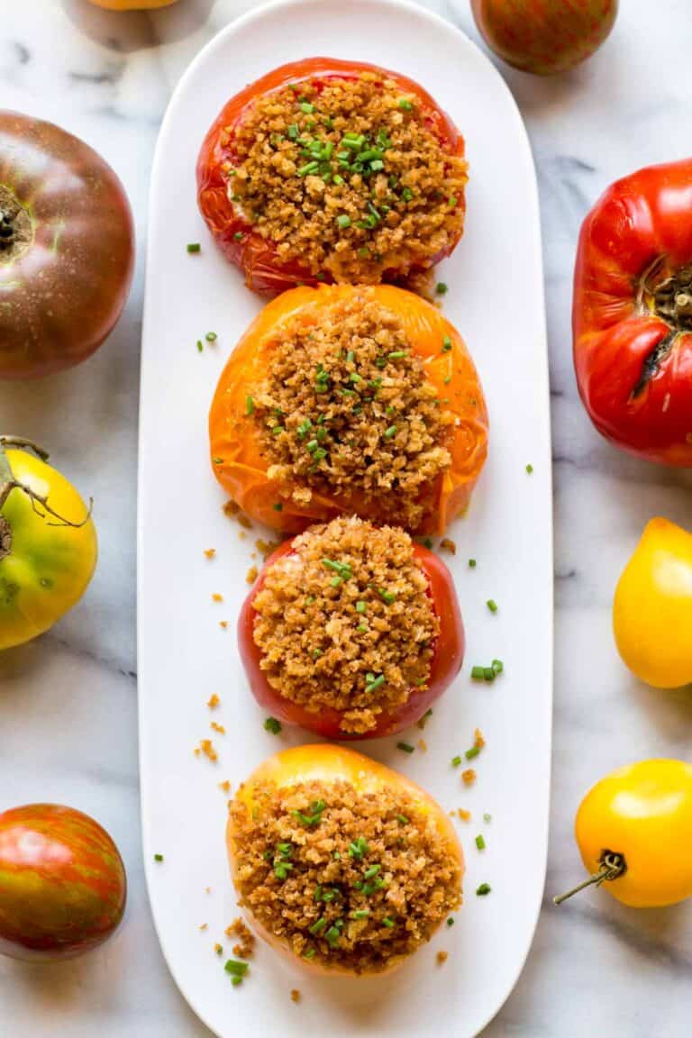 Overhead shot of a long white plate with four red and yellow tomatoes with breadcrumbs on top.