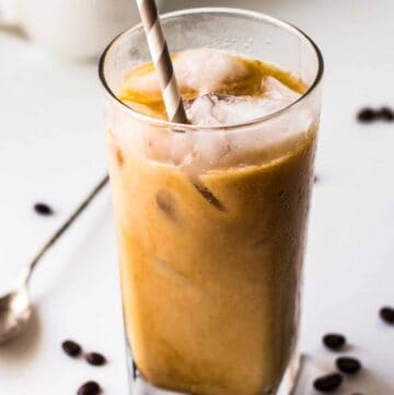 A tall glass of iced coffee with a straw and coffee beans in the background.