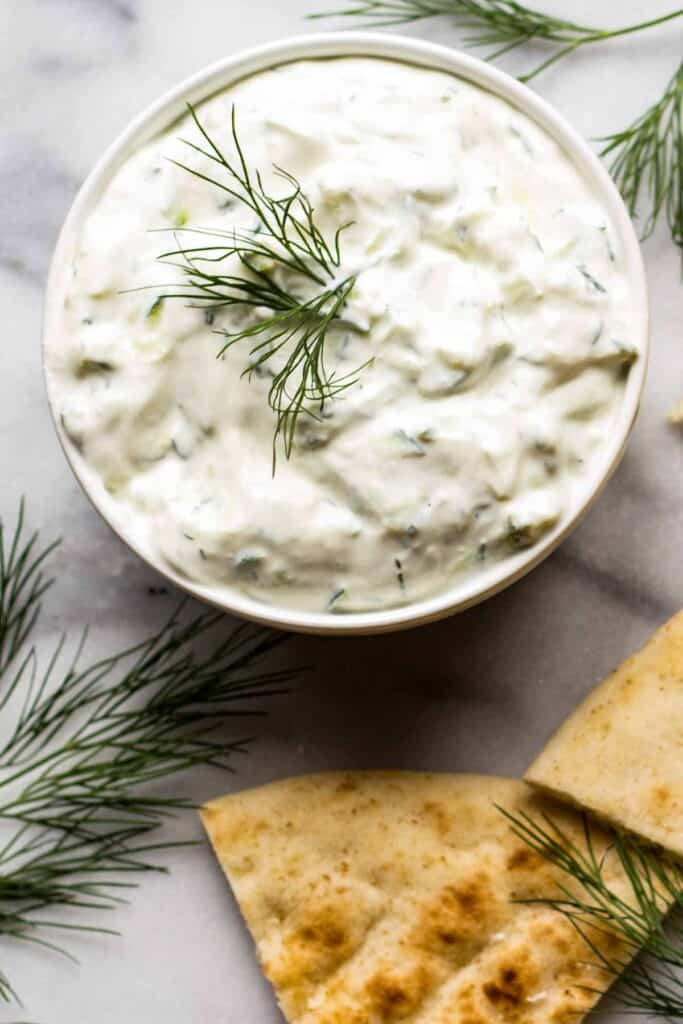 Overhead shot of a bowl of Tzatziki Sauce with dill sprigs and pita triangles.