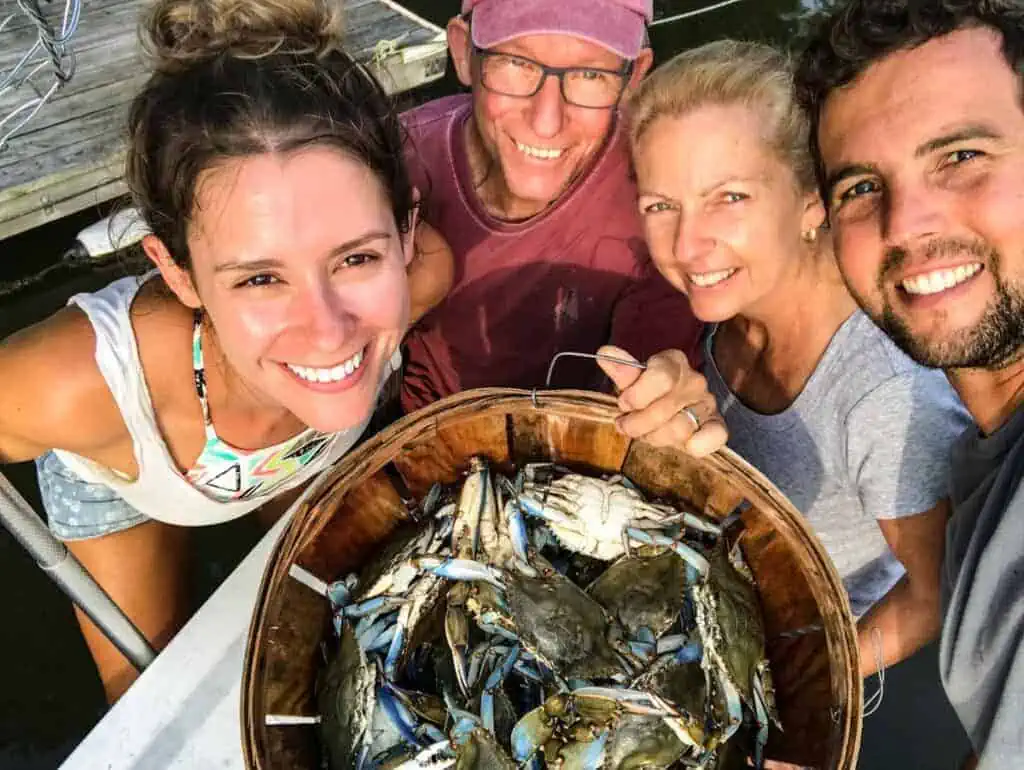 overhead shot of 4 people smiling, holding up a basket of blue crabs
