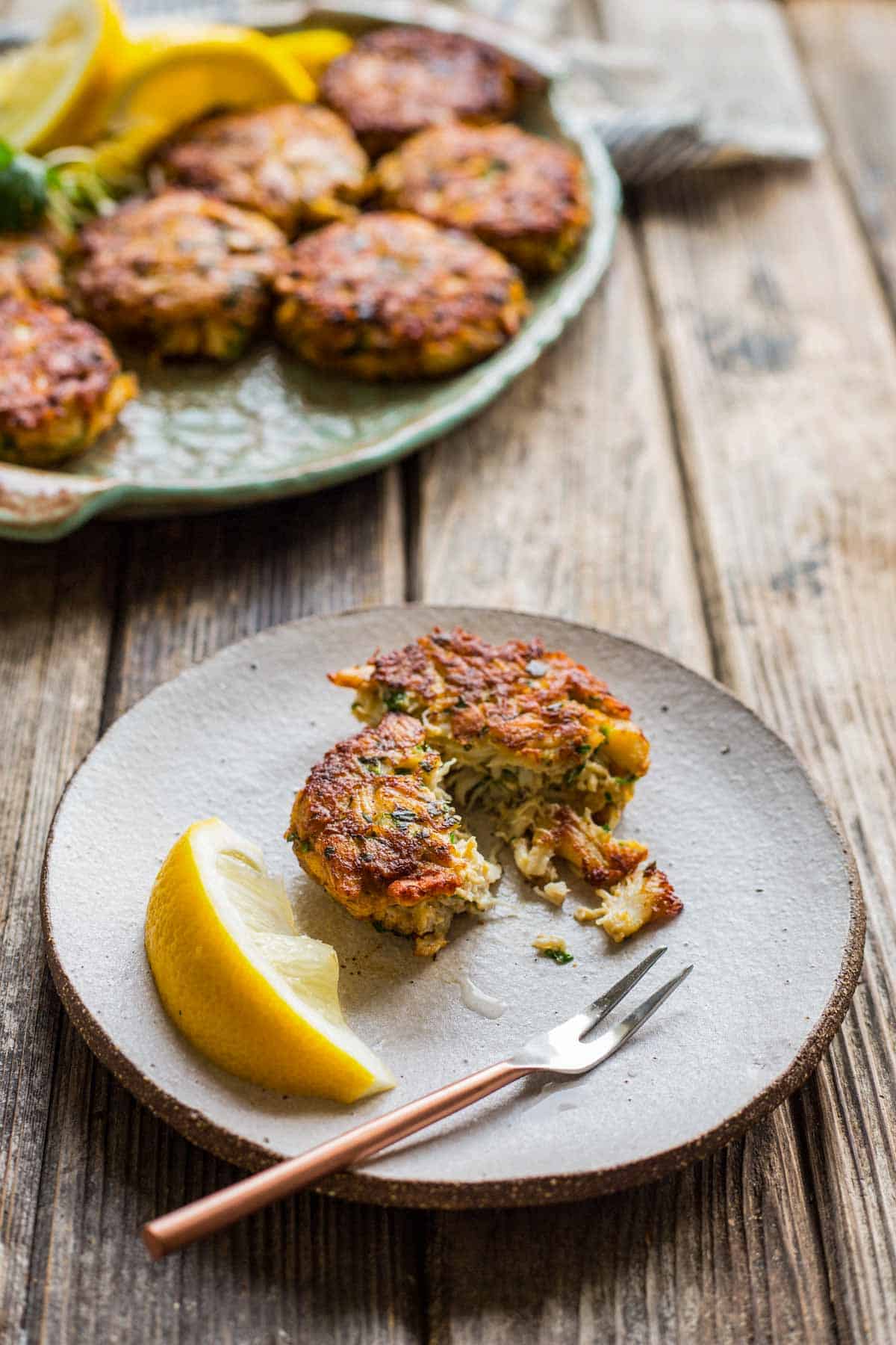 side view of a small plate with a broken up crab cake, lemon wedge and small fork