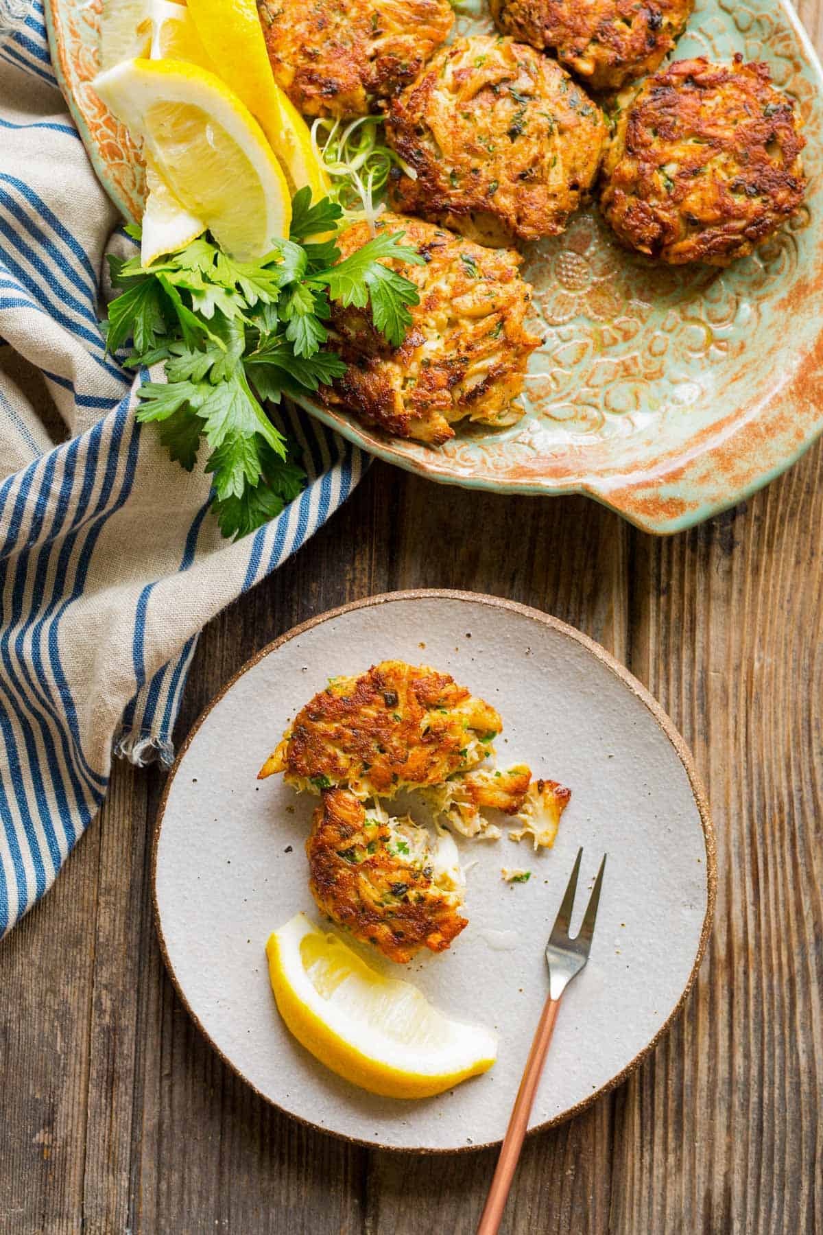 overhead shot of a small plate with a broken up crab cake, lemon wedge and small fork