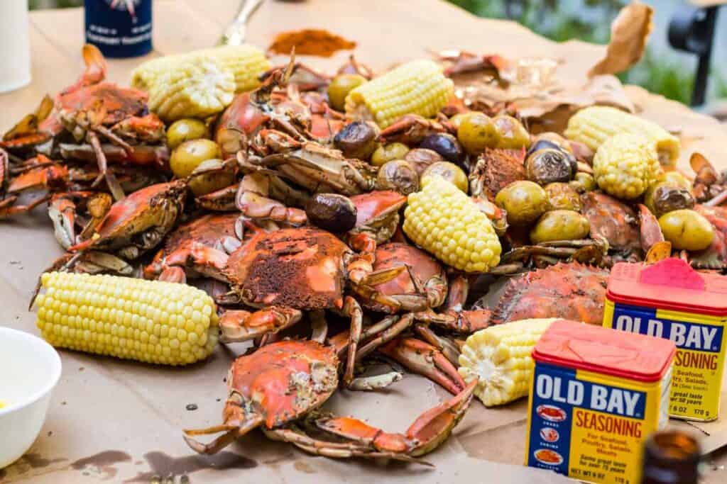 Horizontal photo of cooked crabs and corn with cans of Old Bay seasoning.