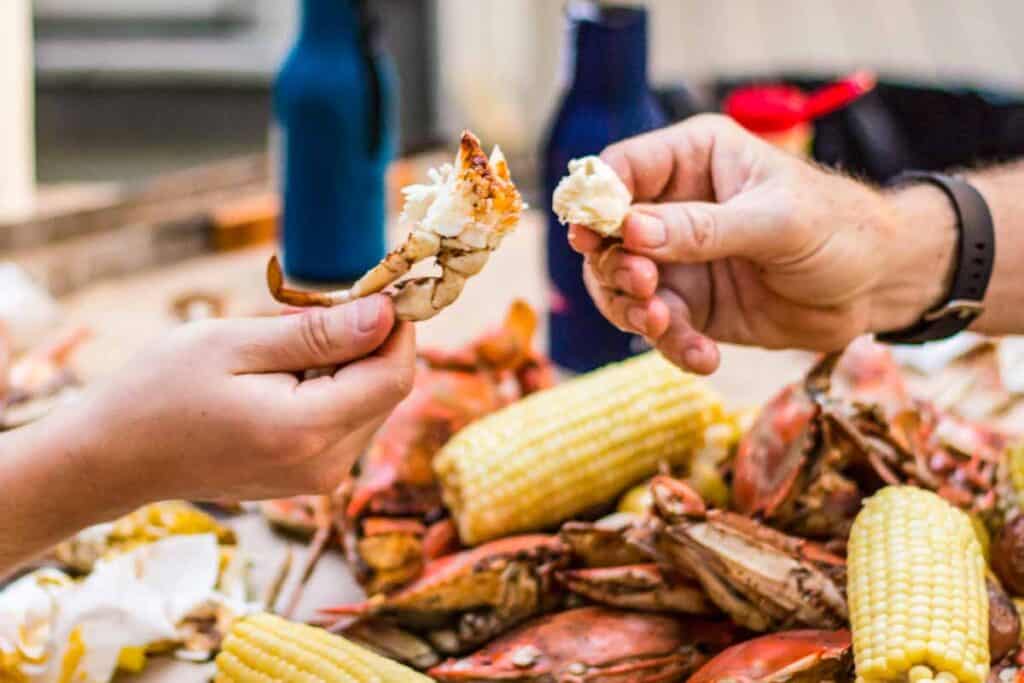 Two hands holding up pieces of jumbo lump crab meat over top of a pile of crabs and corn.