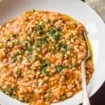 Close up of a shallow white bowl with tomato risotto and fresh herbs.