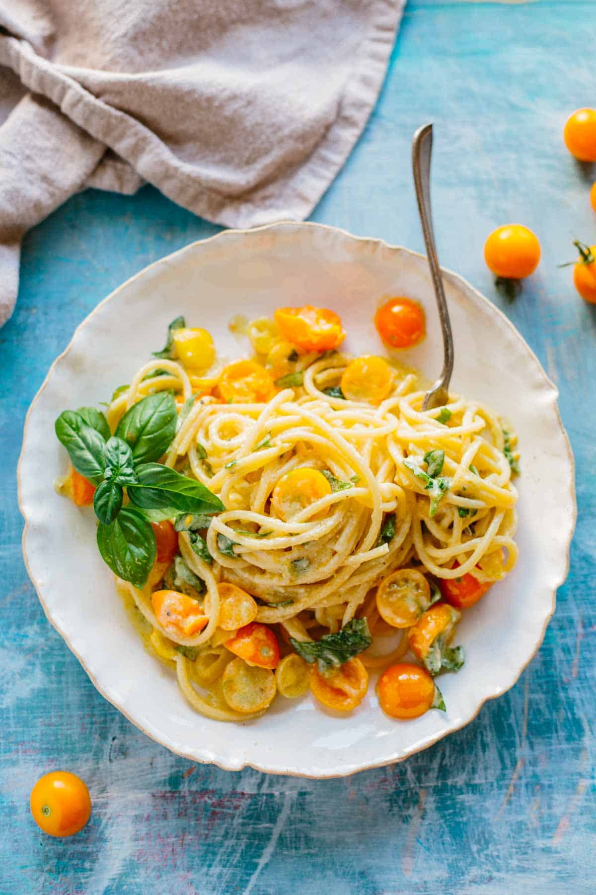 Overhead shot of a bowl of pasta with orange tomatoes, basil and a fork.